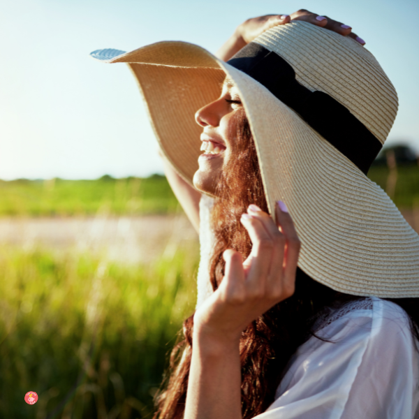 Woman enjoying the outdoors holdin a large hat.