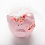 Pink piggy bank wearing a veil and a post it with wedding budget written on it on a white table background.